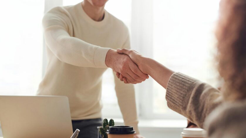 Close-up of professionals shaking hands over coffee in a modern office.